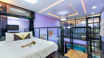A modern hotel room with a bed, a glass balcony, and a view of a swimming pool.