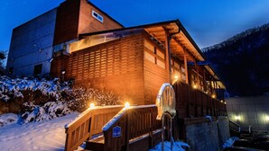 A wooden cabin with a wooden staircase leading to a porch, surrounded by snow. - Vista Hill Pool Villa (Gapyeong)