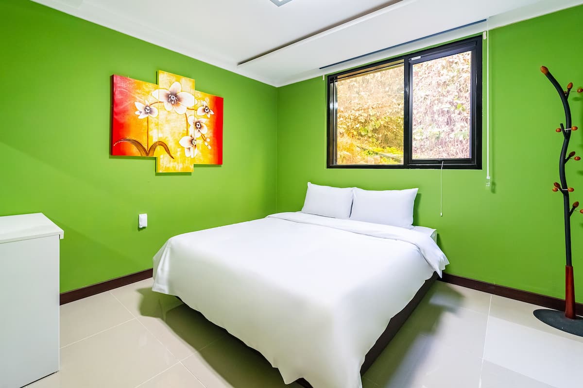 Ein Schlafzimmer mit einem Bett, grünen Wänden, einem Fenster und einem Gemälde.