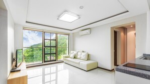 A spacious living room with a large sliding glass door leading to a balcony, a white sofa, and a kitchen area with granite countertops. - Vista Hill Pool Villa (Gapyeong)