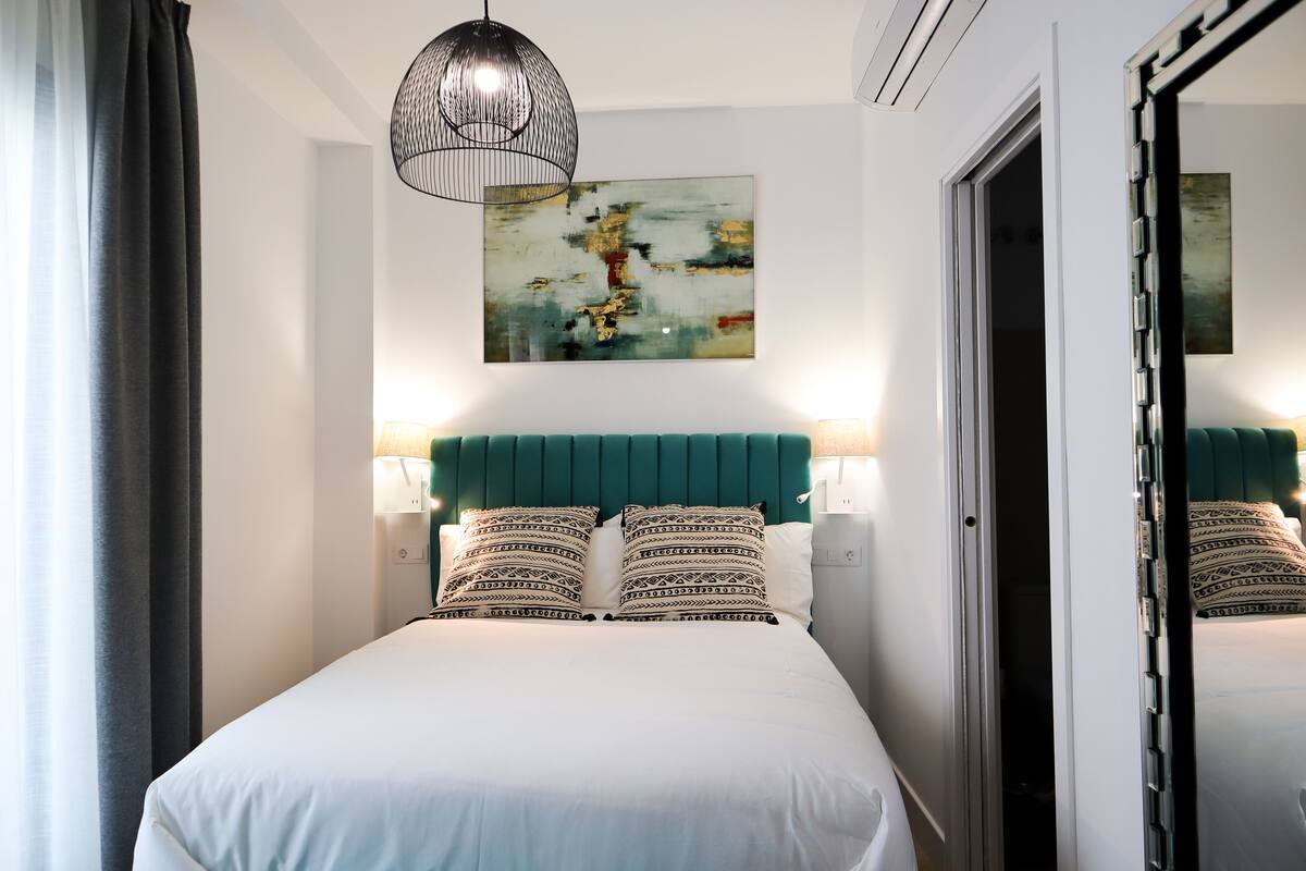 A modern hotel room with a bed, a teal headboard, and a large abstract painting on the wall.