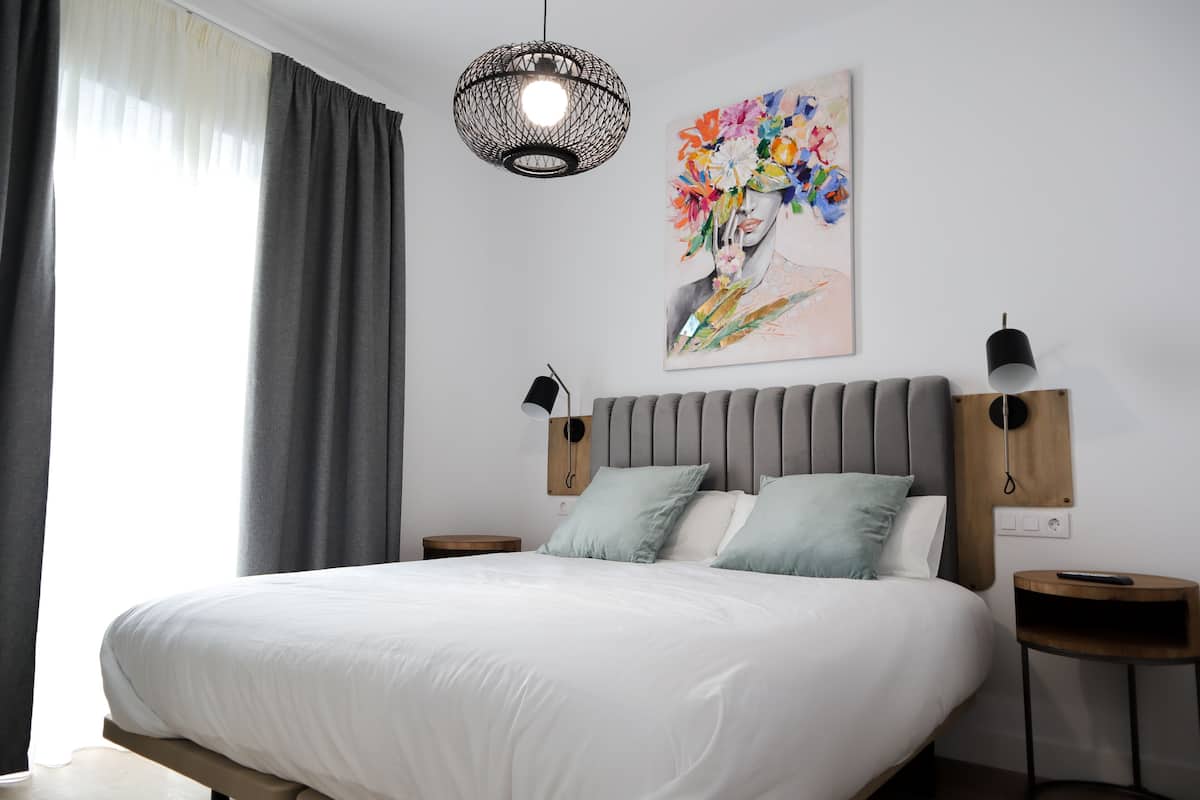 A modern bedroom with a large bed, two bedside tables, a wall-mounted lamp, and a colorful artwork.