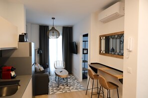 Ein modernes Hotelzimmer mit einer Küchenzeile, einem Essbereich mit Tisch und Stühlen, einem Sofa, einem gemusterten Teppich und einem großen Spiegel.