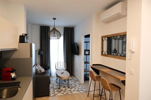 Une chambre d’hôtel moderne dotée d’une kitchenette, d’un coin repas avec une table et des chaises, d’un canapé, d’un tapis à motifs et d’un grand miroir.