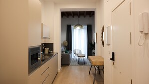Eine moderne Küche mit integriertem Mikrowellenherd, ein Essbereich mit Holztisch und Stühlen sowie ein Wohnbereich mit Sofa und Lampe.