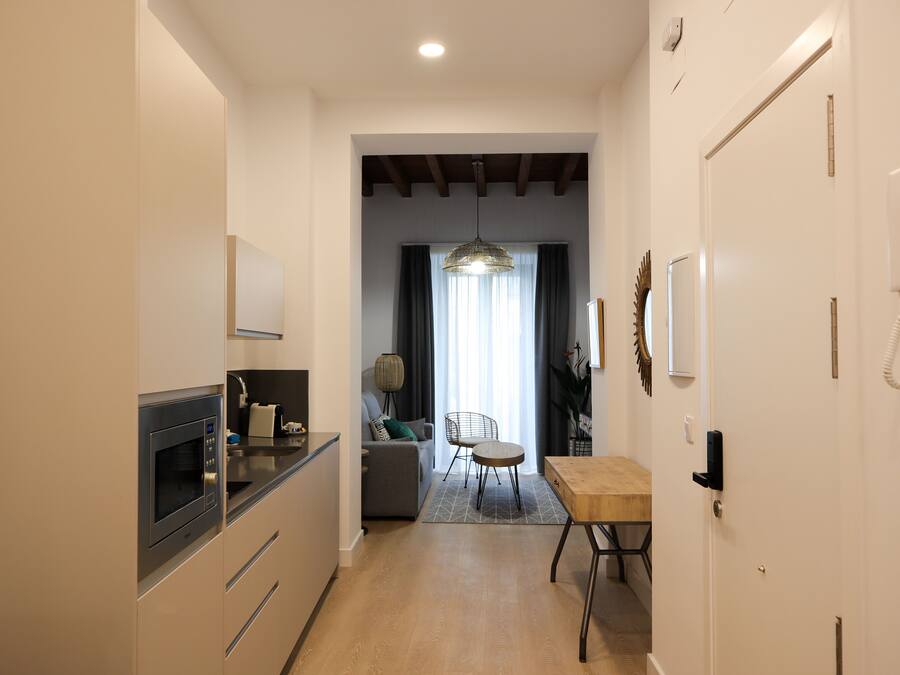 A modern kitchen with a built-in microwave, a dining area with a wooden table and chairs, and a living space with a sofa and a lamp.
