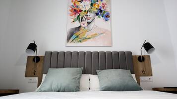 Un dormitorio moderno con un cabecero tapizado gris, una colcha blanca y dos lámparas de noche.