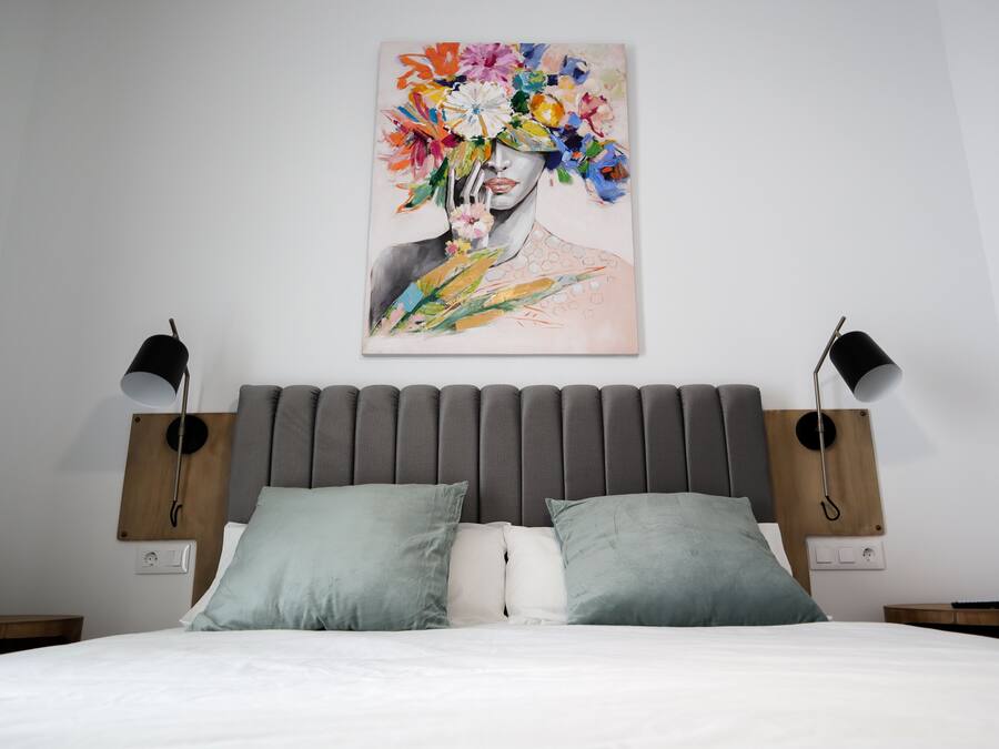 Un dormitorio moderno con un cabecero tapizado gris, una colcha blanca y dos lámparas de noche.