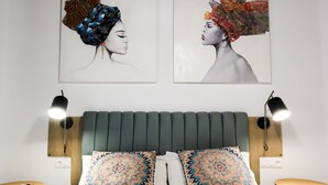 Ein Schlafzimmer mit einem Bett, zwei Kissen, zwei Nachttischen, zwei Wandlampen und zwei gerahmten Kunstwerken an der Wand.