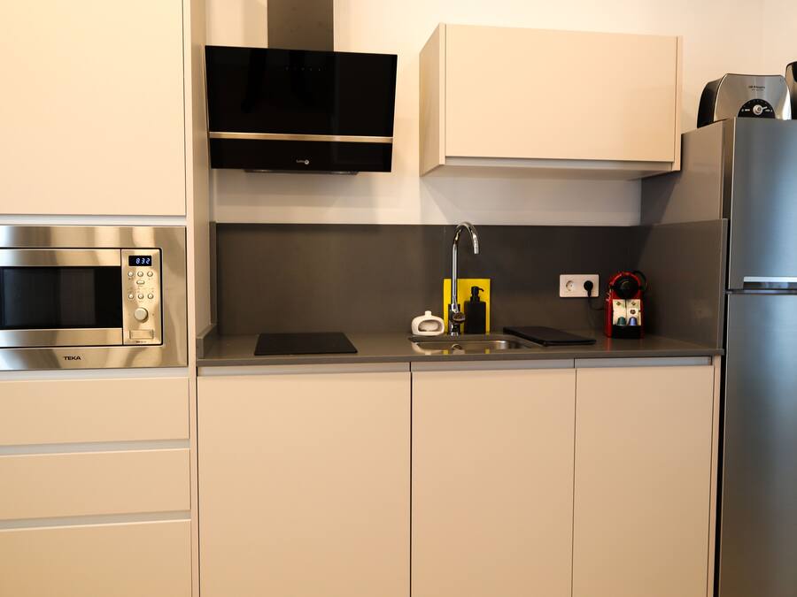 Uma cozinha moderna com eletrodomésticos de aço inoxidável, incluindo micro-ondas, forno e geladeira. Há um exaustor embutido e uma pia com torneira.