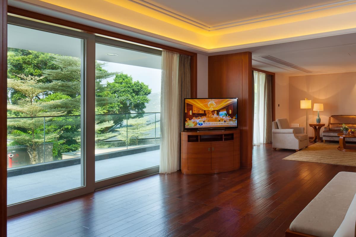 Amplia habitación de hotel con una cama grande, televisor, zona de comedor y vistas al exterior.