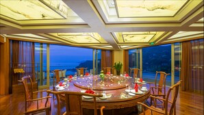 Una mesa redonda con sillas, dispuesta para una comida, en una habitación con ventanas amplias y vista al mar.