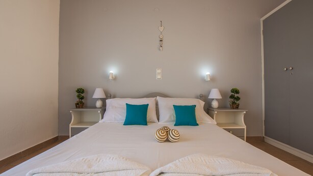 Un letto rifatto con lenzuola bianche e cuscini color acquamarina, due comodini con lampade e un lampadario a parete.
