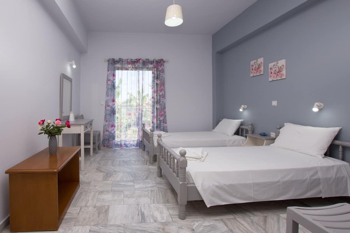 Un dormitorio con dos camas, un escritorio, una silla, un espejo y una ventana con cortinas florales.