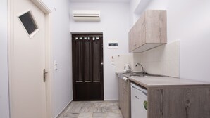 Una cucina compatta con una porta scura, pareti bianche e pavimento piastrellato.