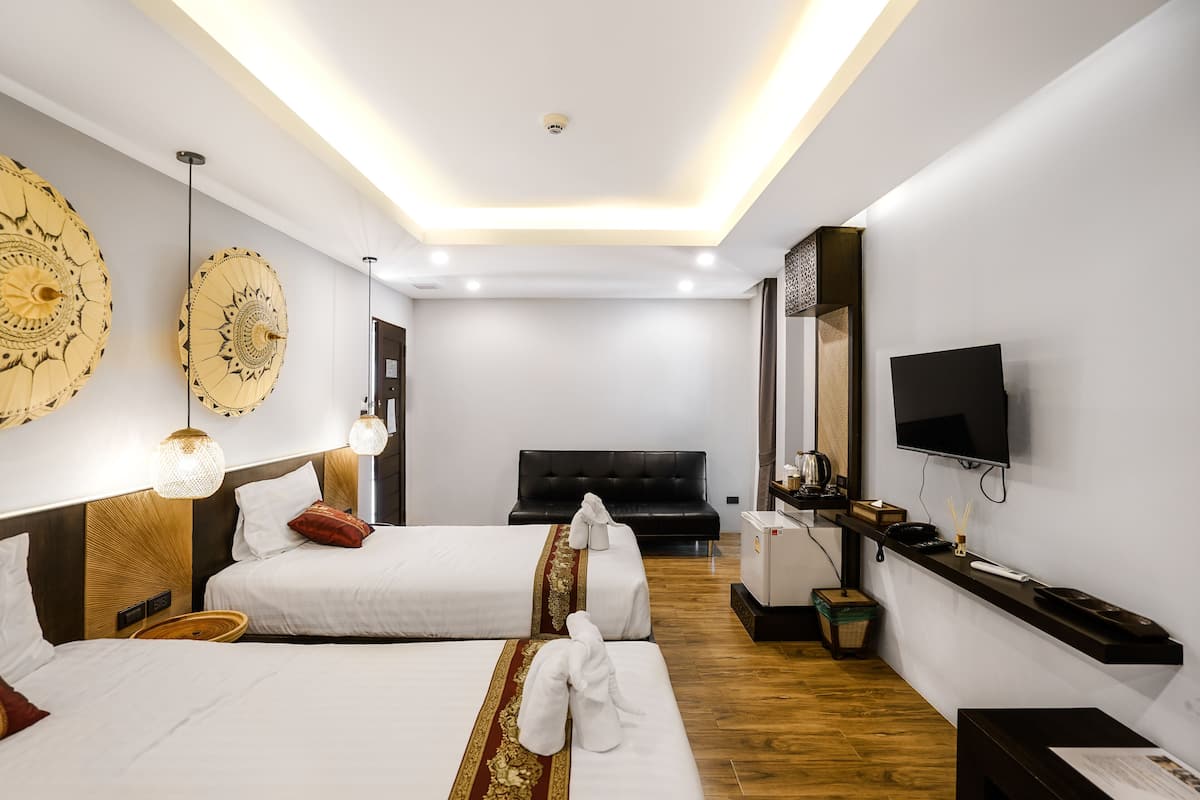 Habitación de hotel con dos camas, televisión, minibar y decoración en las paredes.