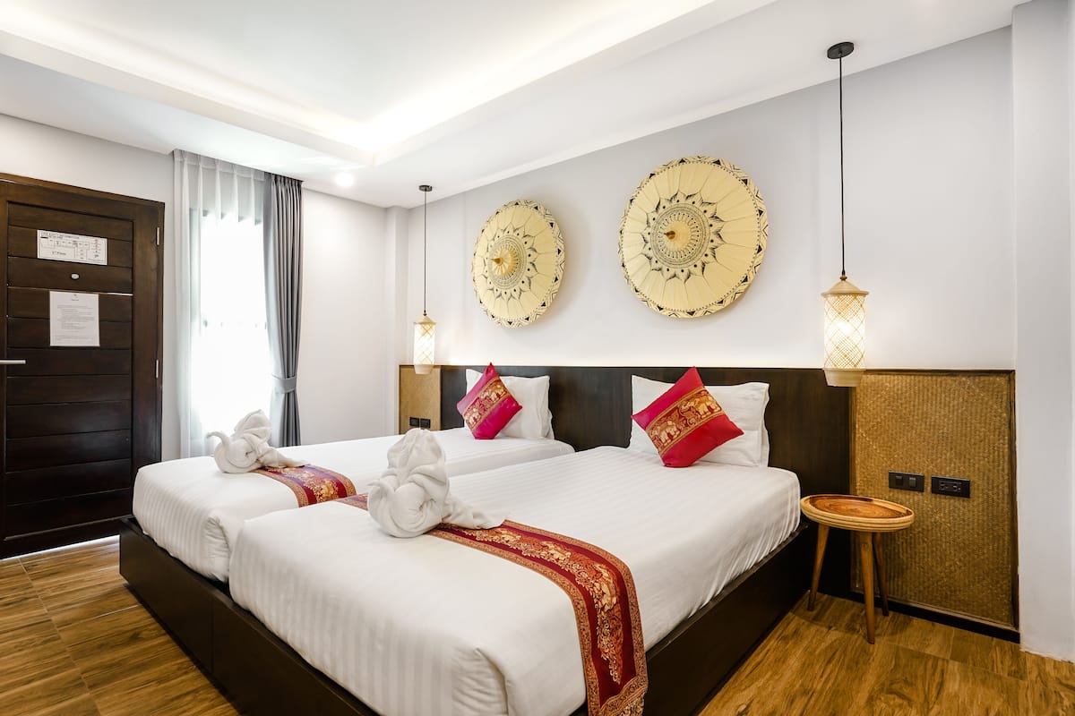 Una habitación de hotel con dos camas, piso de madera, un amplio ventanal con cortinas y detalles decorativos en la pared.