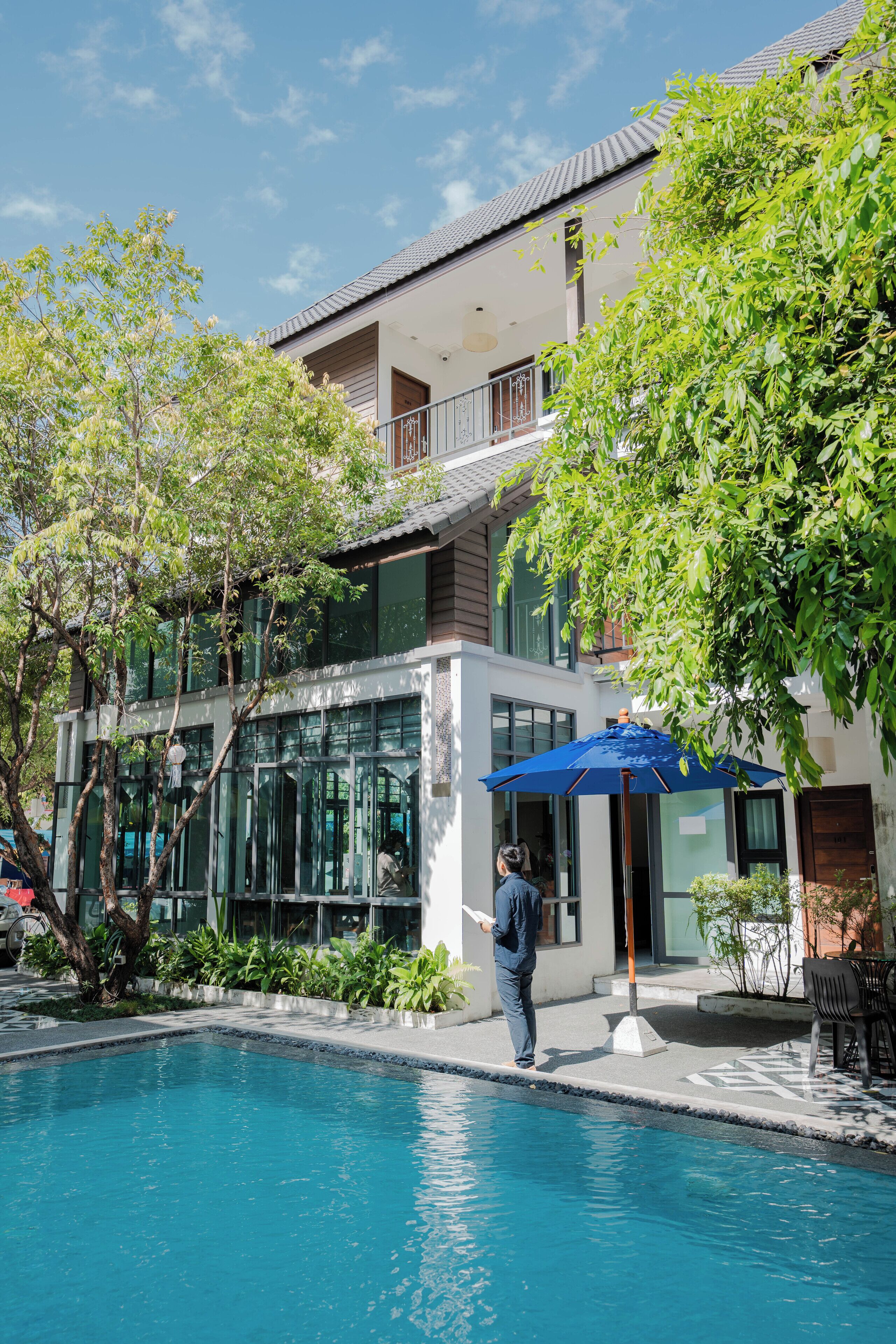 A modern building with a swimming pool, glass doors, and a blue umbrella.