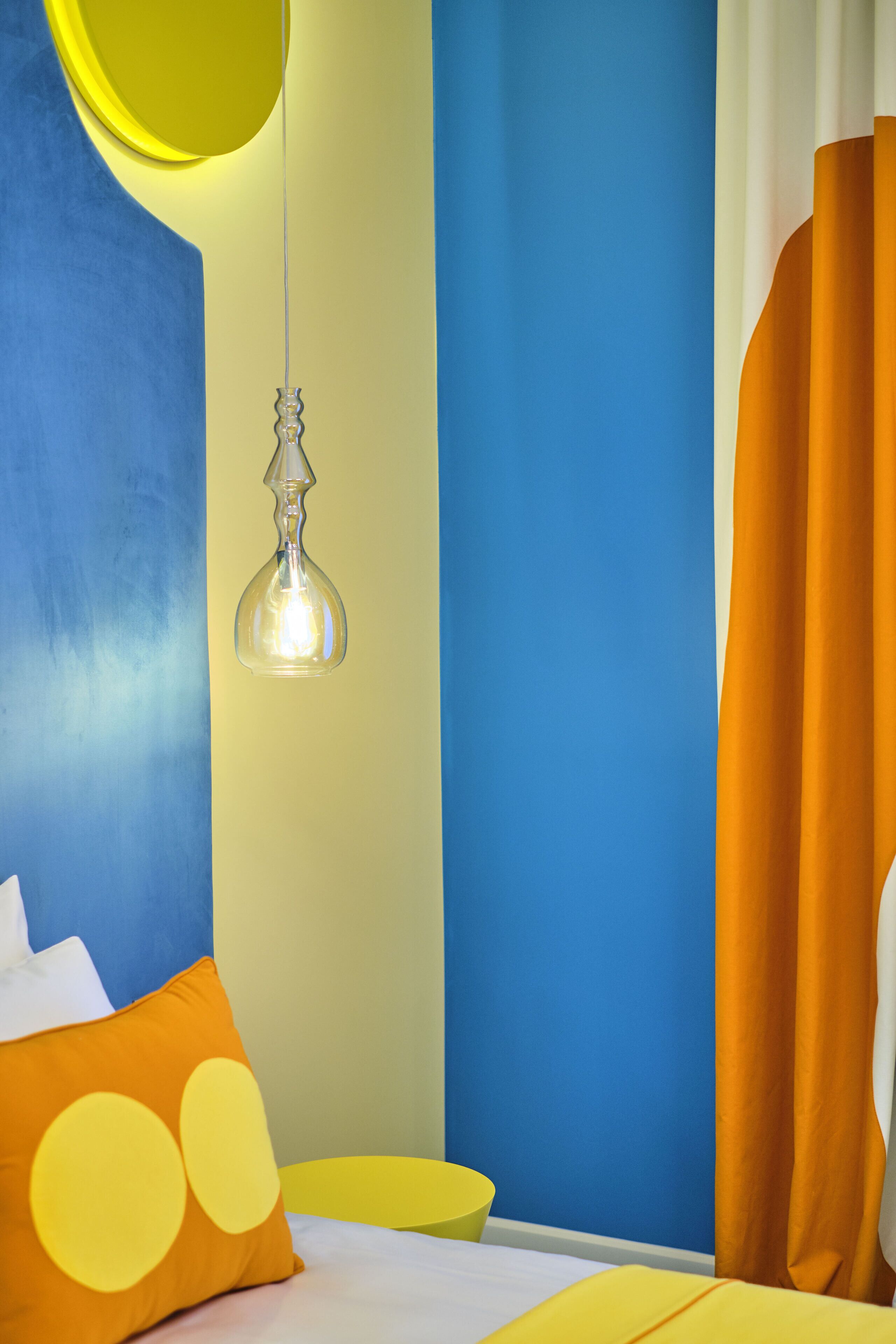 A room with a bed, a hanging light fixture, and a yellow pillow.