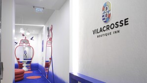 Um corredor com carpete azul, uma estrutura de recreação vermelha e uma parede com o logotipo do 'Vilacrosse Boutique Inn'.