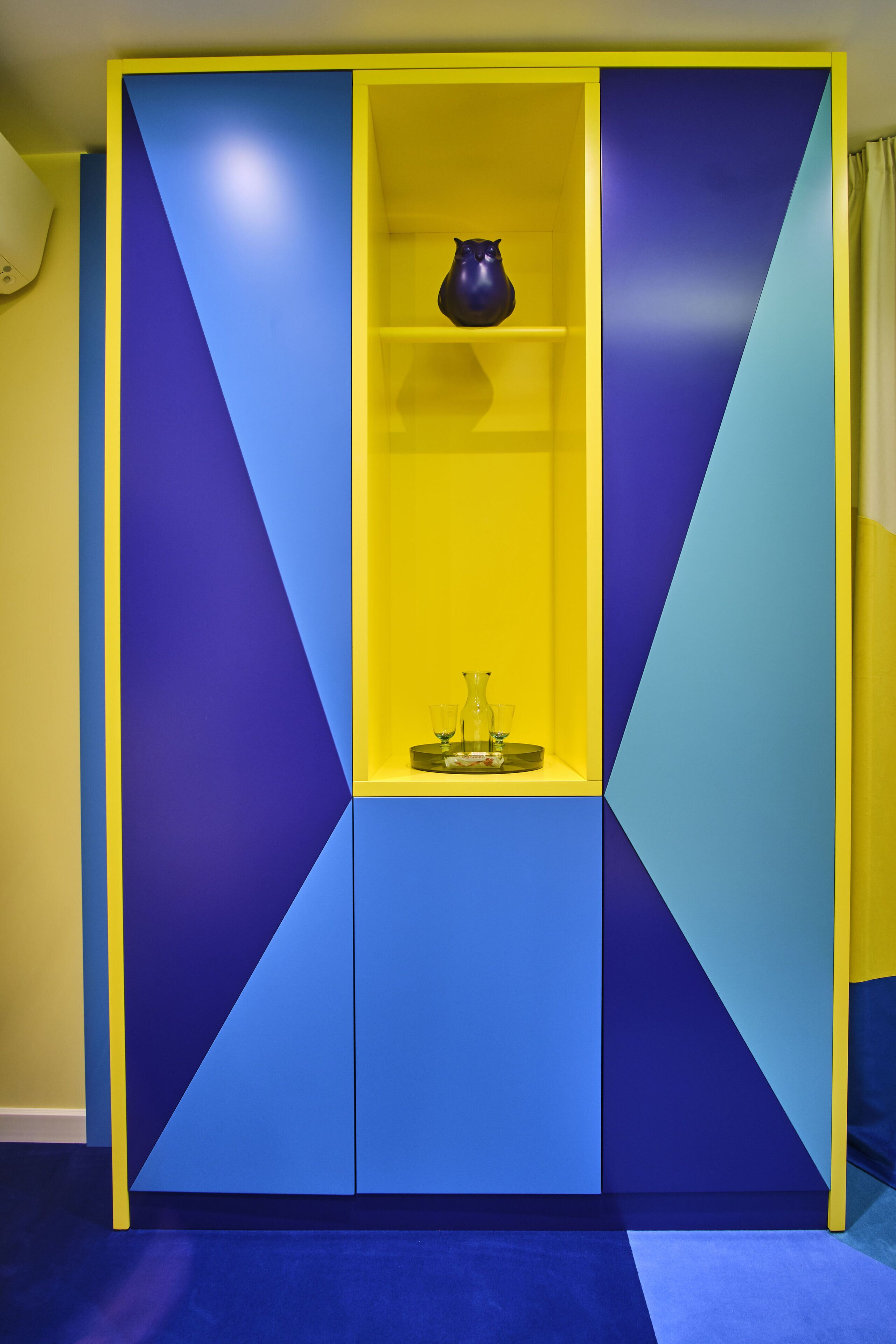 Een kamer met een inbouwkast met een geometrisch patroon en een klein plankje met decoratieve objecten.