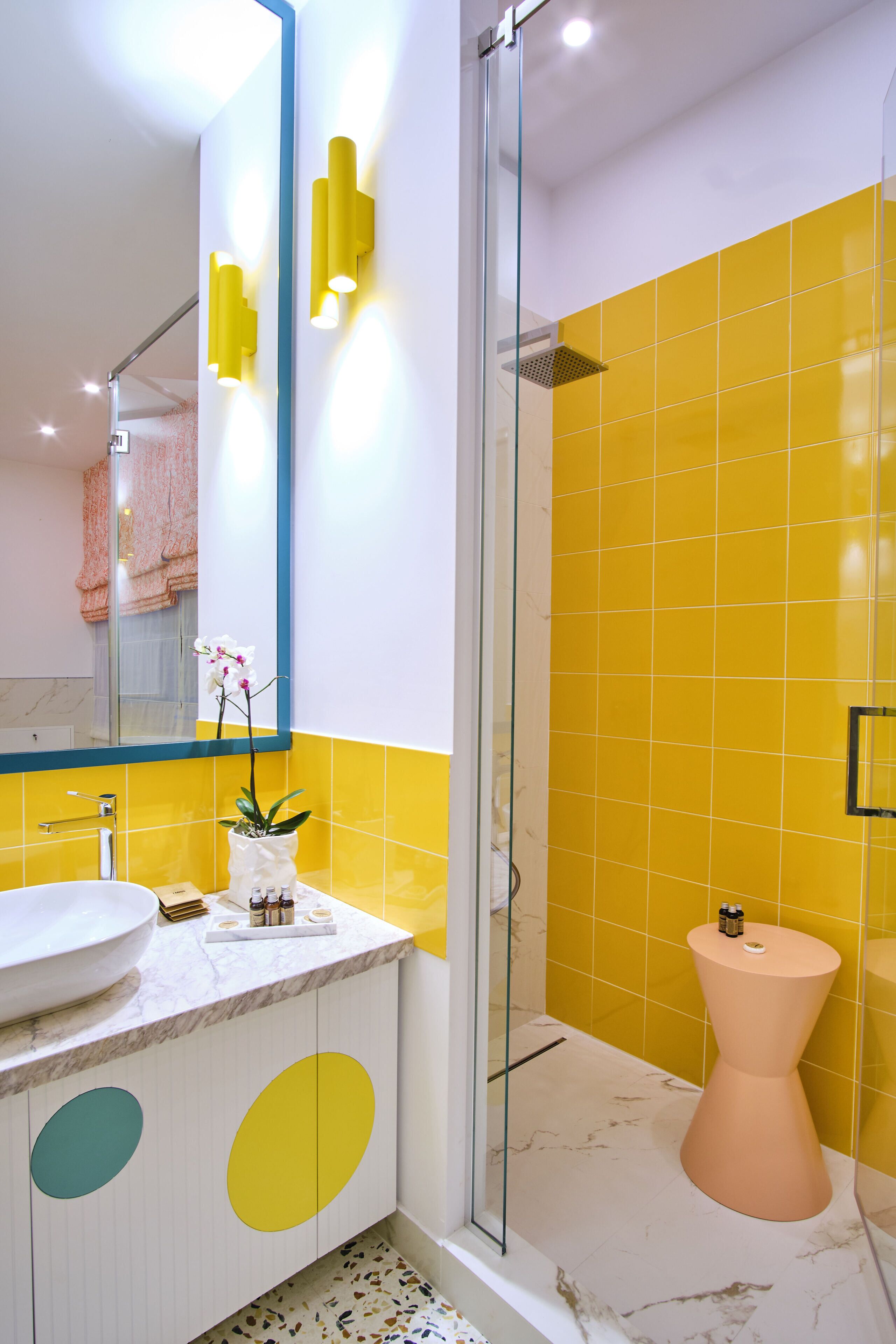 Une salle de bain moderne avec une douche à parois de verre, un lavabo blanc et un mur recouvert de carreaux jaunes.
