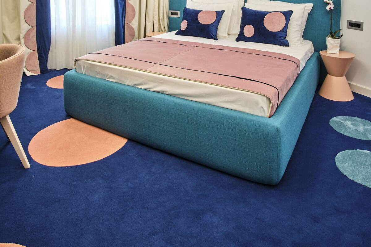 A modern bedroom with a teal headboard, a large bed with pink and white bedding, and a circular ceiling light fixture.