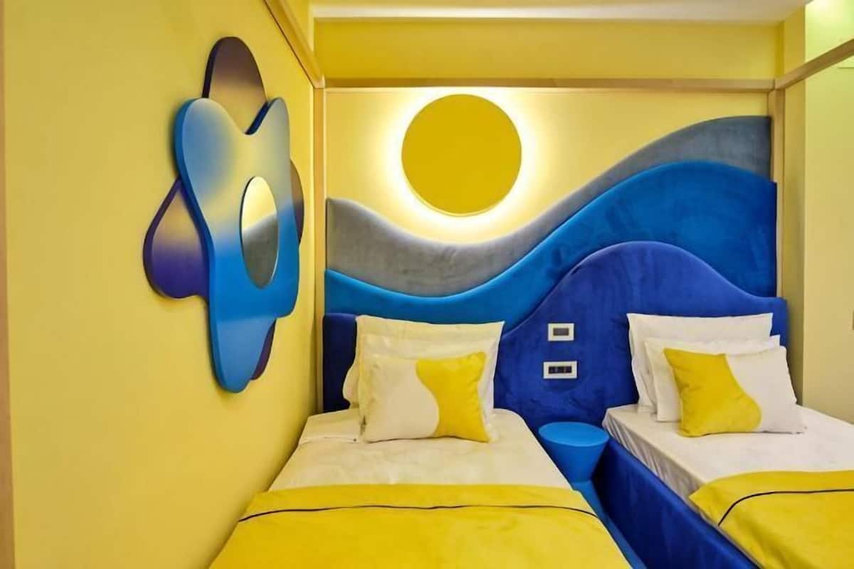 A room with a bed, two bedside tables, and a wall with a circular light fixture.