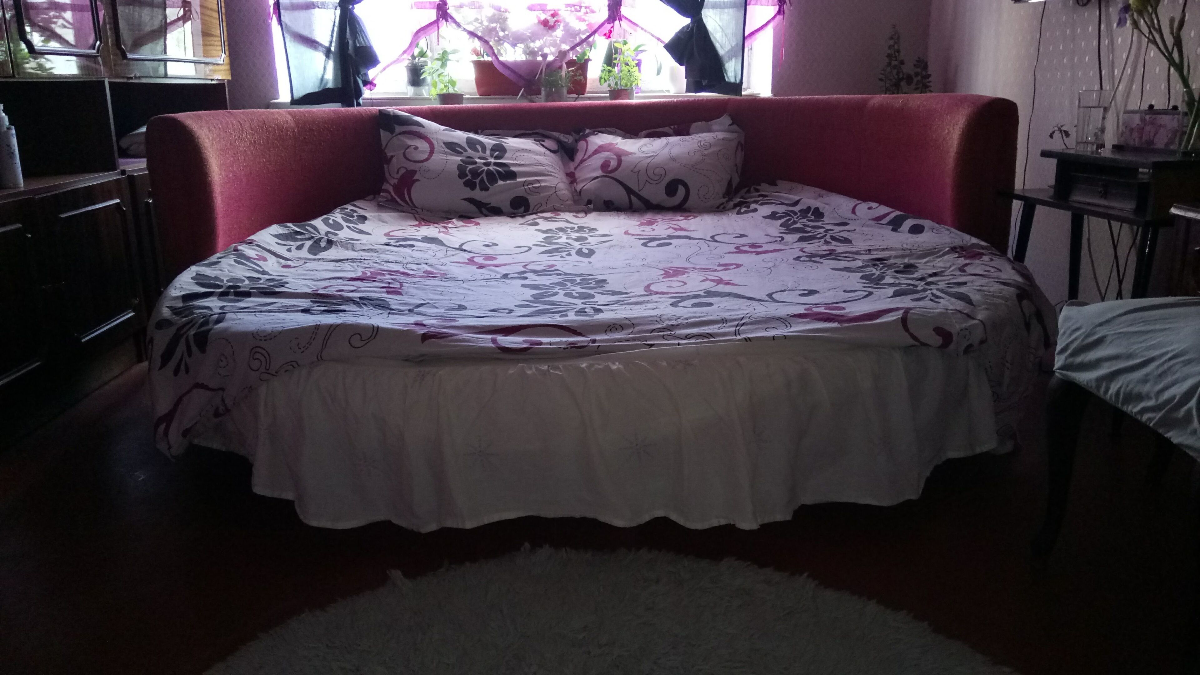 Une chambre à coucher avec un grand lit, une tête de lit rouge et une fenêtre avec des rideaux.