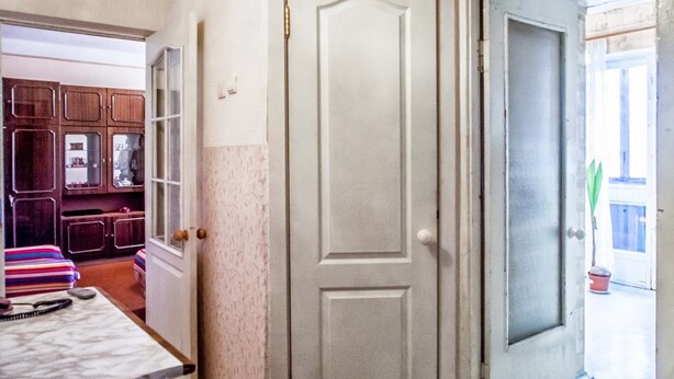 Un pasillo con una puerta blanca, un mueble de madera con puertas de cristal y un sofá a rayas.