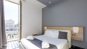 A modern hotel room with a large bed, a wooden headboard, and a view of the city through a balcony. - Palace Napoli (Naples)