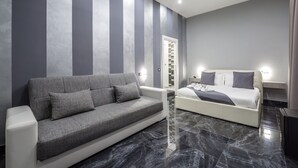 A modern hotel room with a grey sofa, a white bed, and a marble floor. - Palace Napoli (Naples)