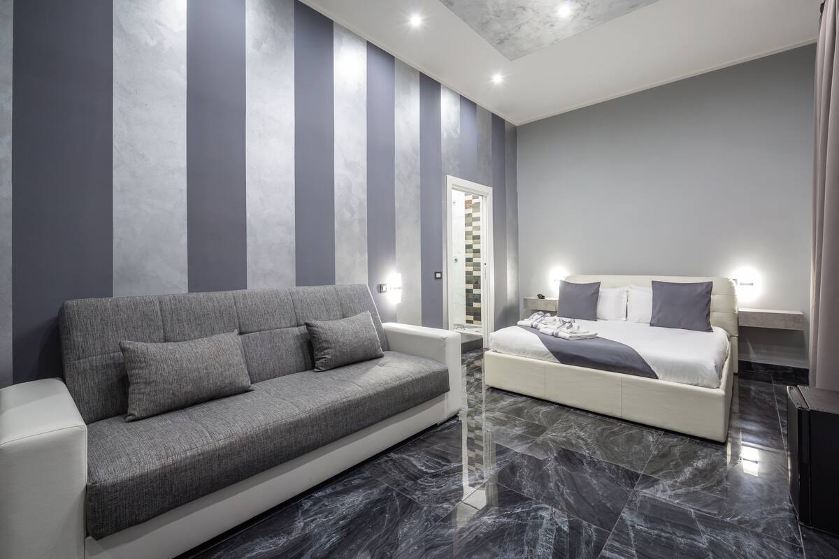 A modern hotel room with a grey sofa, a white bed, and a marble floor.