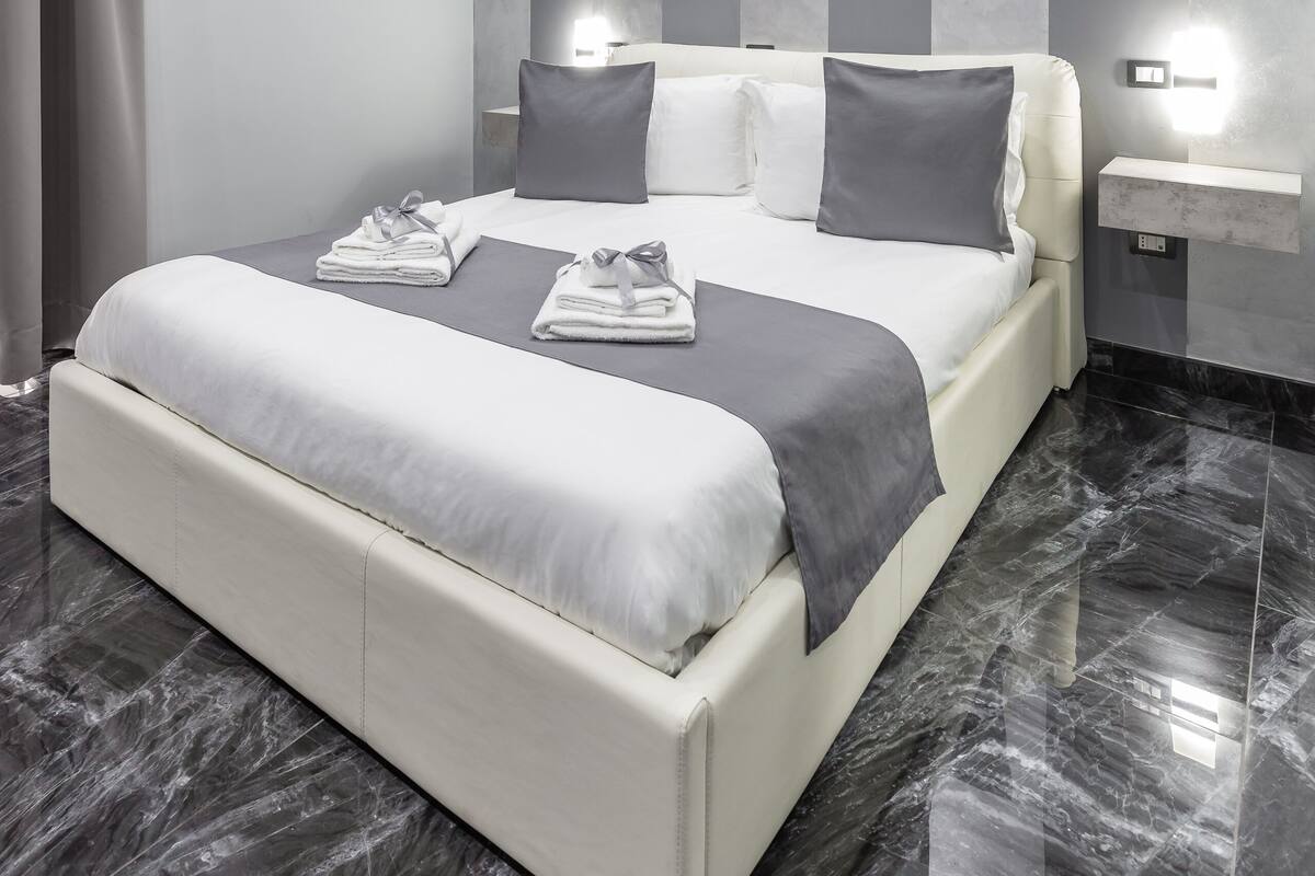 A modern bedroom with a large bed, grey and white striped walls, a marble floor, and a ceiling light fixture.