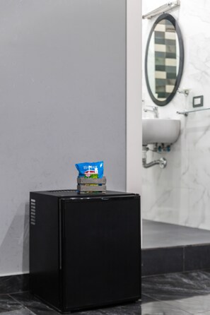 Un refrigerador negro compacto en un baño, con un espejo y un lavamanos al fondo.
