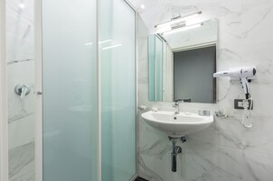 Un bagno moderno con box doccia in vetro, lavabo bianco e asciugacapelli fissato alla parete.