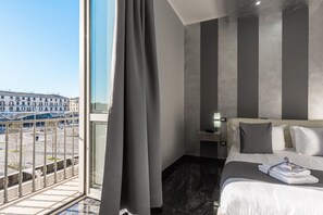 Habitación de hotel moderna con un gran ventanal, una cama con ropa blanca y vistas a la ciudad.