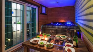 A dining area with a table set for a meal, a hot tub with blue lighting, and a view of a room with a bed and a window. - Sky Wind and Star SPA Pension (Pocheon)
