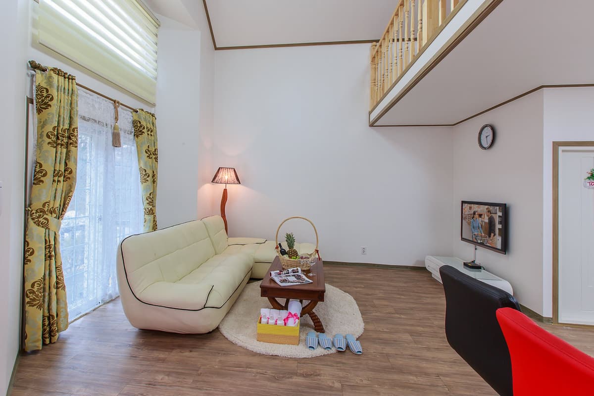 A living room with a sofa, a small table with a lamp, a basket with fruits, and a television.