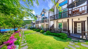 A two-story building with a balcony, a stone pathway, and a pool in the background. - Sky Wind and Star SPA Pension (Pocheon)