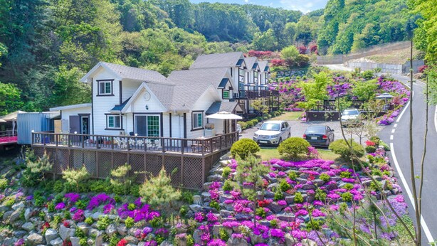 A residential area with houses, a paved road, and a landscaped garden with colorful flowers. - Sky Wind and Star SPA Pension (Pocheon)