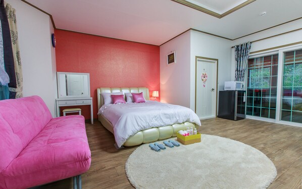 A bedroom with a bed, a pink chair, a white bedside table, a mirror, a white door, and a window with curtains.