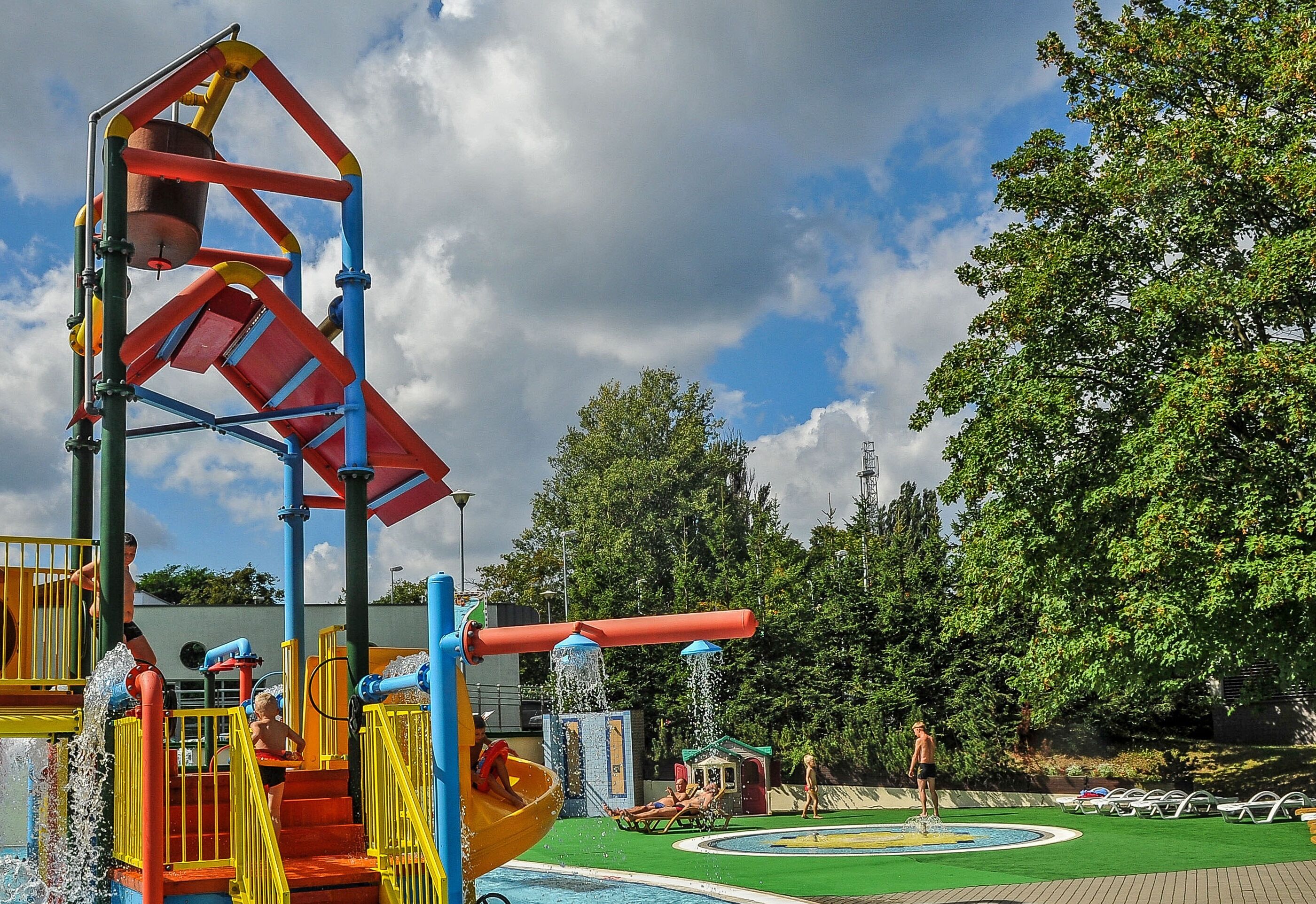A water park with a colorful play structure, a pool, and a green lawn area.