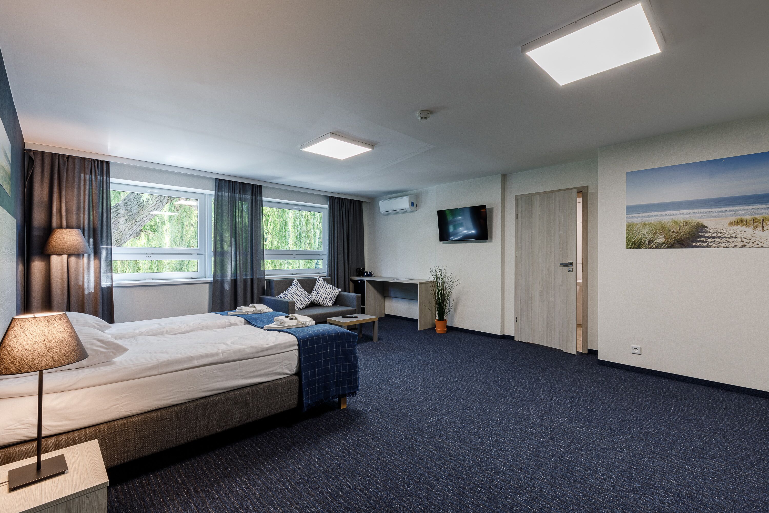 A hotel room with a bed, desk, chair, and a TV on the wall.