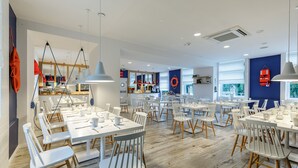 A modern dining area with white tables and chairs, a kitchen in the background, and a blue accent wall with a circular design. - Aqua House (Sopot)