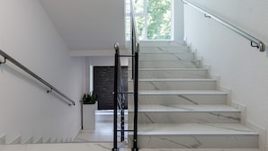 A modern staircase with marble steps and metal handrails, leading to a landing with a potted plant. - Aqua House (Sopot)