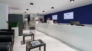A modern reception area with a blue textured wall, a reception desk, and a staircase in the background. - Aqua House (Sopot)