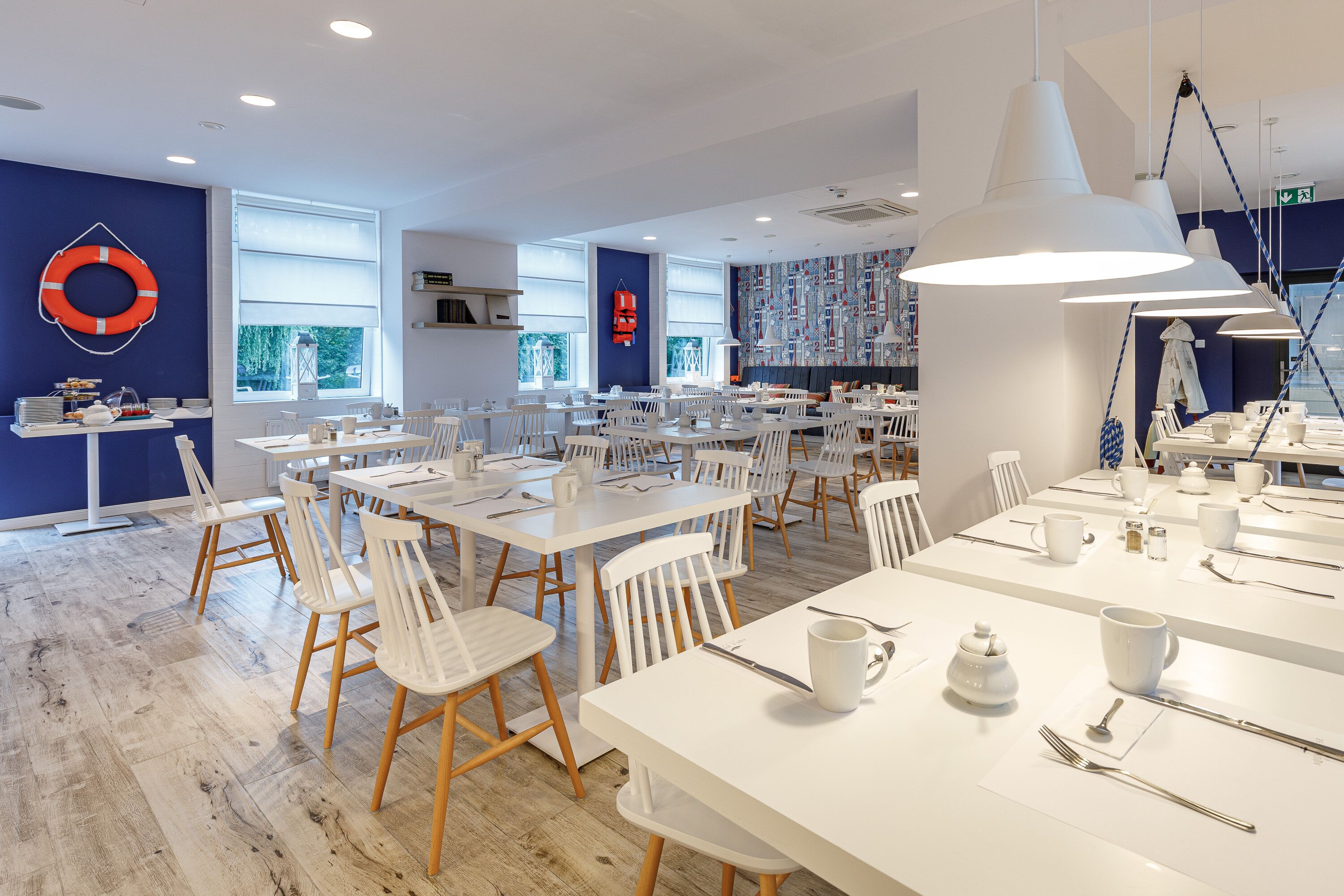 Un espace de restauration moderne avec des tables et des chaises blanches, un anneau de sauvetage accroché au mur et de grandes fenêtres.