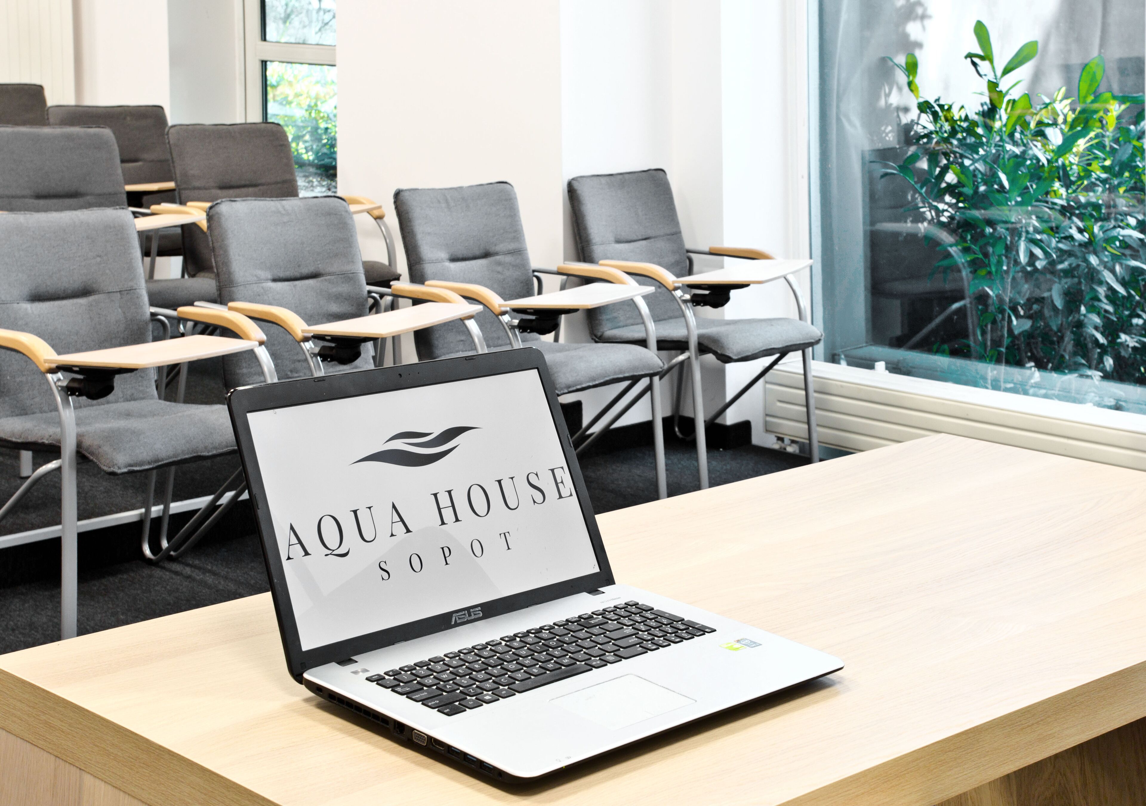Een laptop op een bureau met een bordje met de tekst 'AQUA HOUSE Sopot'.