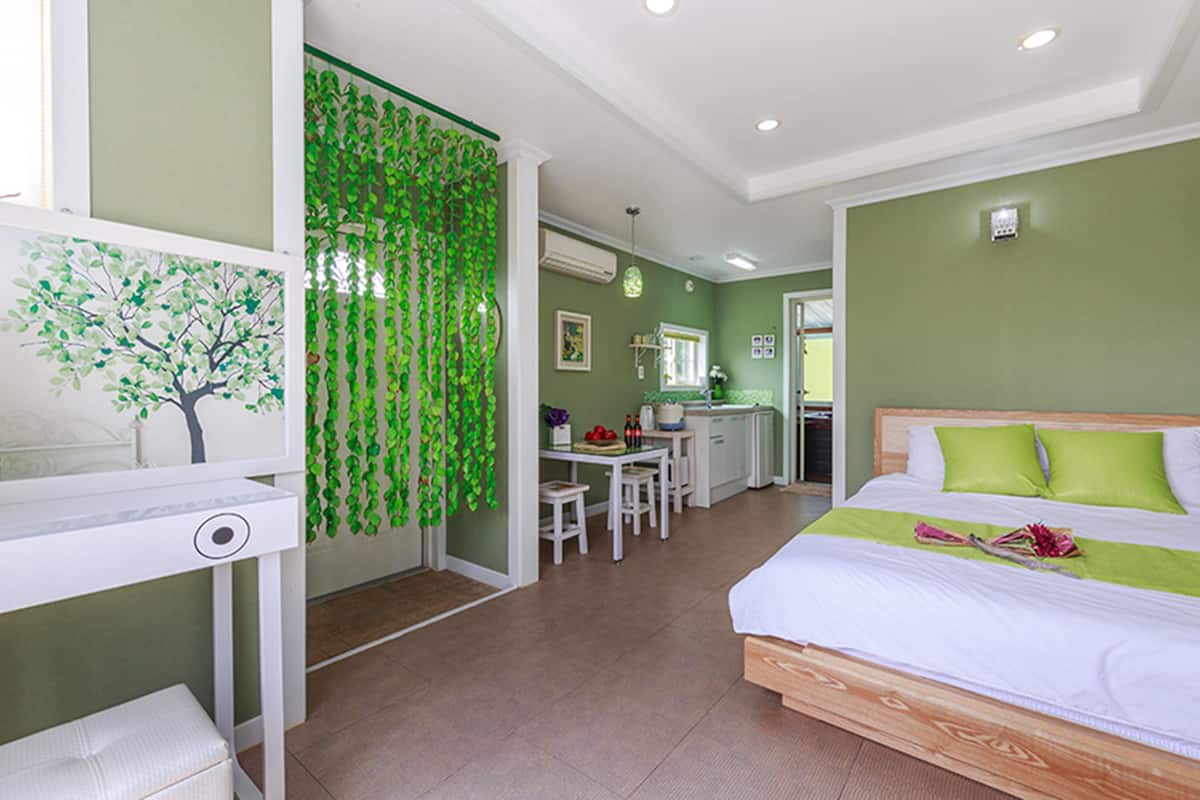 A bedroom with a bed, a desk, and a kitchenette.